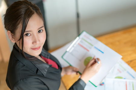 Business woman holding a pencil is working with business chart graph checking infomation inside is working with business chart graph checking infomation insideの写真素材