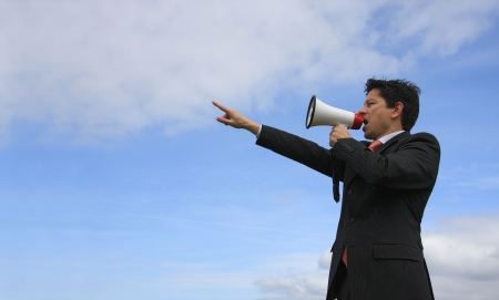 A business man giving an order with a megaphone with a blue sky as Backgroundの写真素材
