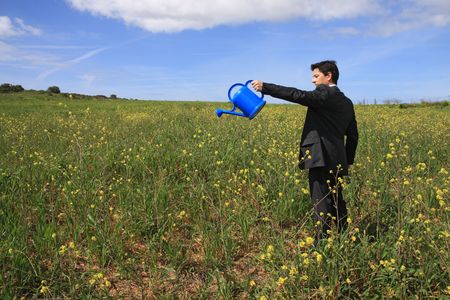Young business man with a blue watering can in a fieldの写真素材