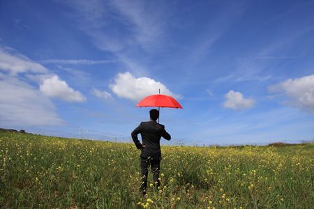 Business man with an open umbrella symbolizing protection on the fieldの写真素材