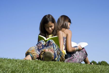 Two young girls reading isolated on blue skyの写真素材