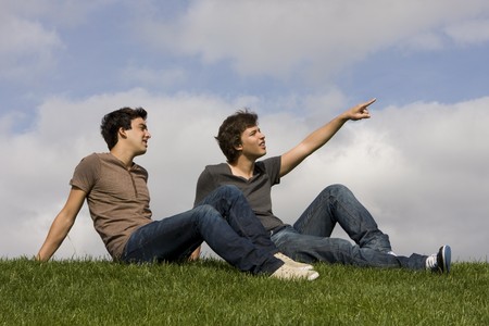 Two friends sit on the grass looking upの写真素材