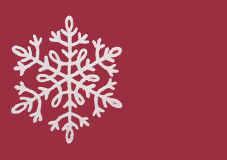 Shiny white snowflake isolated on a red background with space for textの写真素材