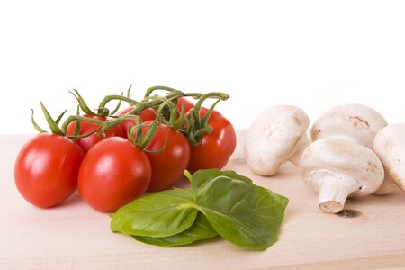 Basil leaves, red tomatoes and mushrooms on a wooden cutting boardの写真素材