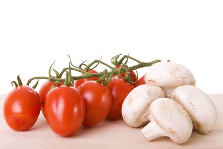 Many mushrooms and cherry tomatoes on a wooden cutting boardの写真素材