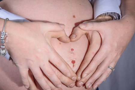 A pregnant mum's tummy with her's and her partners hands in a heart shape