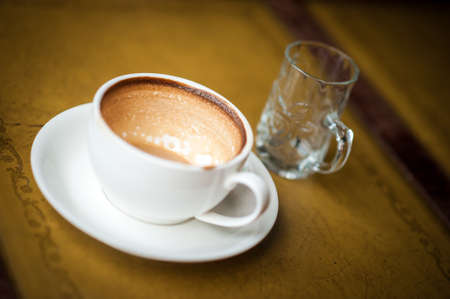 A cup of coffee with flower pattern in a white cup on vintage leather background