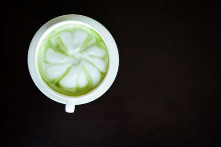 Hot milk green tea (selective focus) in the white cup on the dark wooden table.の写真素材