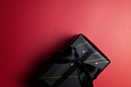 Top view of black christmas gift box with red and black ribbons isolated on red background. Shopping...