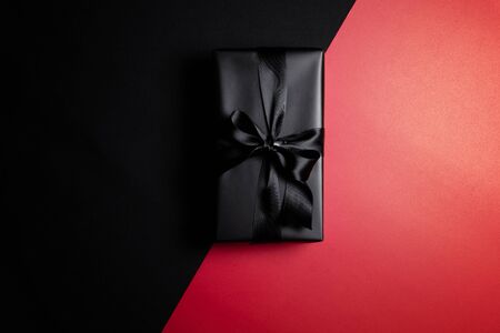Top view of black gift box with black ribbons isolated on red and black background. Shopping concept boxing day and black Friday sale composition.の写真素材