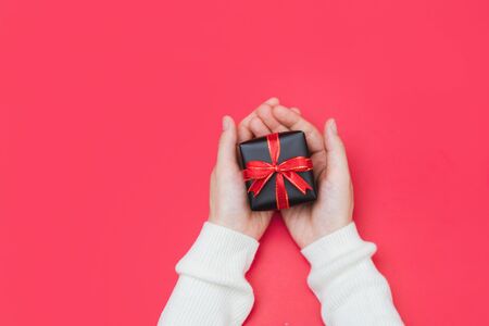Close up shot of female hands holding a small gift wrapped with red ribbon. Holiday present concept with copy space, banner. の写真素材