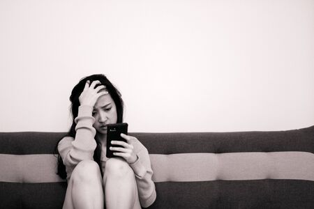 An asian woman getting anxiety and depression after checking news in mobile phone about global pandemic. Lockdown mental health. Coronavirus outbreakの写真素材