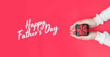 Close up shot of daughter hands holding a small gift wrapped with red ribbon. Father's day present concept with text. Shallow depth of field with focus on the little box.の写真素材