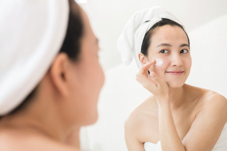 Happy young Asian woman applying face lotions while wearing a towel and touching her face.の写真素材