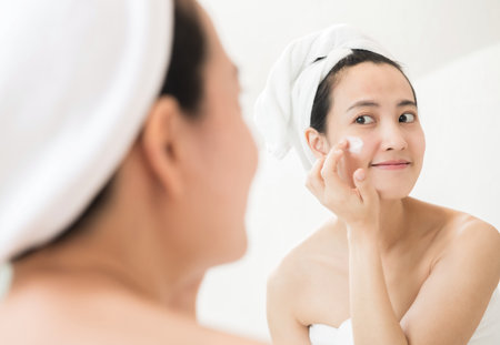 Happy young Asian woman applying face lotions while wearing a towel and touching her face.の写真素材
