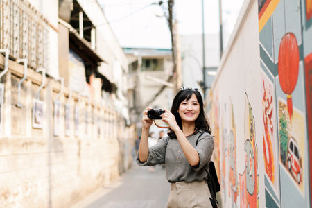 Young Asian woman backpack traveler using digital compact camera, enjoying street cultural local...