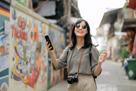 Young Asian woman backpack traveler using mobile phone, enjoying street cultural local art wall.