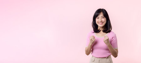 Portrait young beautiful asian woman happy smile with fist up victory gesture expression cheerful her success achievement against pink pastel studio background. Woman day winner celebration concept.の写真素材