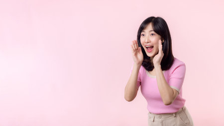 Portrait young beautiful asian woman expression yel scream announce news of communication message or shout loud voice with hand beside mouth gesture isolated on pink pastel background.の写真素材