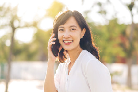 Portrait beautiful young asian woman with smart mobile phone around outdoor nature view in sunny summer dayの写真素材