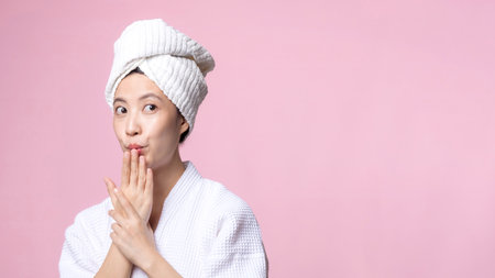Young beautiful asian woman happy with clean face skin in towel and bathrobe, spa suit on pink background. Skincare, treatment, wellness therapy, facial care, beauty female health, cosmetology conceptの写真素材