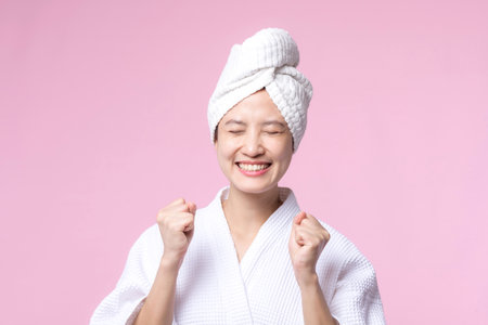 Young beautiful asian woman happy smile face with hand or finger gesture signs in bathrobe and shower towel showing empty space isolated on pink background.の写真素材