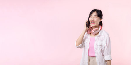 Portrait attractive young asian woman happy smile using smartphone with earphone, headphone isolated on pink studio background. Pretty female person using mobile phone. Music online lifestyle concept.の写真素材