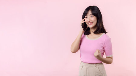 Pretty young asian woman showing success, victory hand gesture while receiving great news from smartphone on pink background. Happy technology, online application, mobile phone advertisement conceptの写真素材