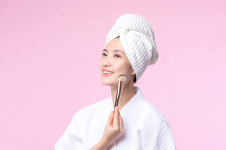 Portrait young happy asian woman with natural make up face holding cosmetic skin powder blusher isolated on pink background. Female apply skincare brush treatment. beauty product, cosmetology concept.の写真素材