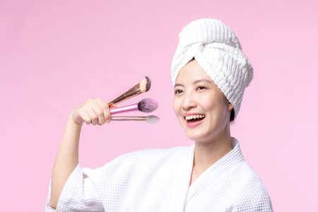 Portrait young happy asian woman with natural make up face holding cosmetic skin powder blusher isolated on pink background. Female apply skincare brush treatment. beauty product, cosmetology concept.の写真素材