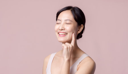 Young beautiful asian woman happy smile with clean face skin in brown bra, spa suit on pink background. Skincare, treatment, wellness therapy, facial care, beauty female health, cosmetology conceptの写真素材