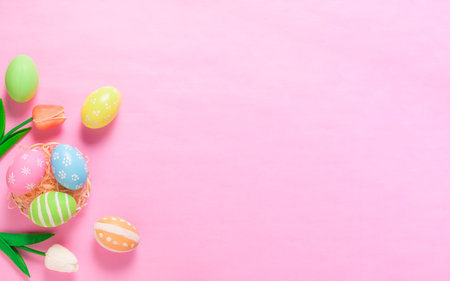 Happy Easter holiday greeting card concept. Colorful Easter Eggs and spring flowers on pastel pink background. Top view, flat lay, copy space.の写真素材