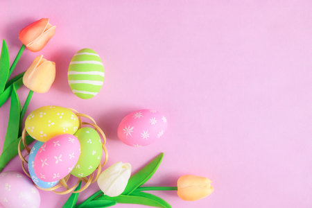 Happy Easter holiday greeting card concept. Colorful Easter Eggs and spring flowers on pastel pink background. Top view, flat lay, copy space.の写真素材