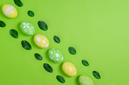Happy Easter holiday greeting card concept. Colorful Easter Eggs and spring flowers on pastel green background. Top view, flat lay, copy space.の写真素材