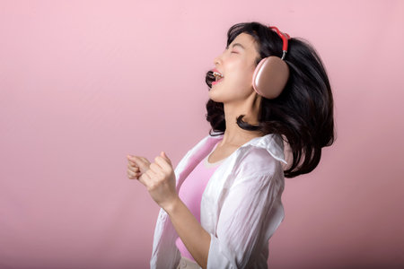 young happy asian woman model with stylish trendy sun glasses enjoy listening music by headphone audio and dancing isolated on pink studio background. technology, girl fashion, accessory concept.の写真素材