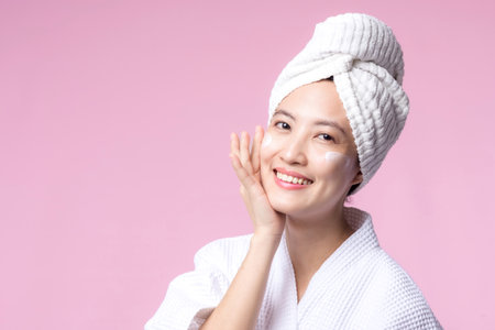 Asian young woman applying facial skincare face cream, cosmetic moisturiser on healthy natural skin make up face. Portrait glowing smile girl person model with care beauty product, spa, cosmetology.の写真素材