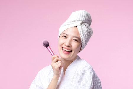 Portrait young happy asian woman with natural make up face holding cosmetic skin powder blusher isolated on pink background. Female apply skincare brush treatment. beauty product, cosmetology concept.の写真素材