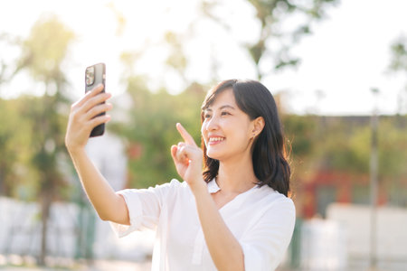 Portrait beautiful young asian woman with smart mobile phone around outdoor nature view in sunny summer dayの写真素材
