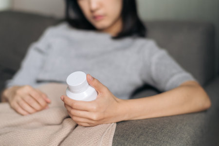 Asian woman with cold and flu reading instructions on a medicine bottleの写真素材