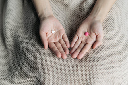 Female hands hold and offer two choice medicine pills capsule for chosen. White and pink candy or meds compare to choose from. Concept indecisiveness or decision making.の写真素材