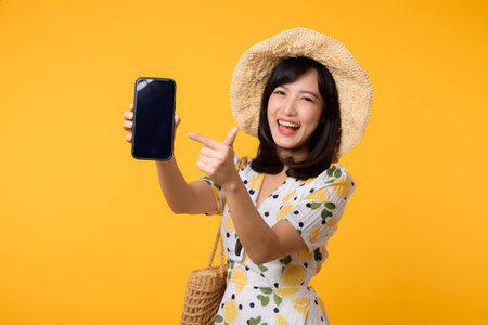 Portrait happy asian young woman with springtime dress fashion showing blank mobile application display screen for advertisement isolated on yellow background. Smartphone app technology concept.の写真素材