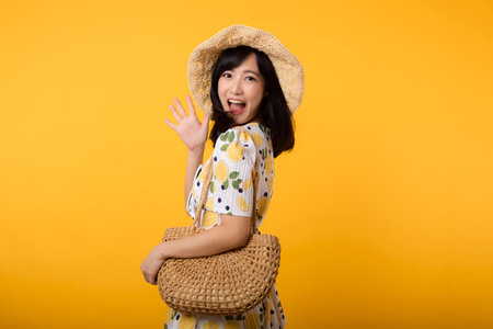 Portrait attractive happy young asian woman with trendy springtime dress, hat, sunglasses fashion and woven bag isolated on yellow background. Summertime sale shopping concept.の写真素材