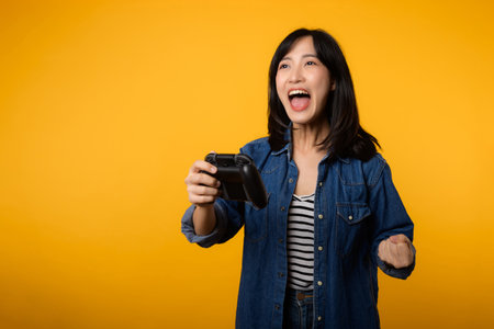 Portrait asian young woman with happy success smile wearing denim clothes holding joystick controller and playing video game. Fun and relax hobby entertainment lifestyle concept.の写真素材