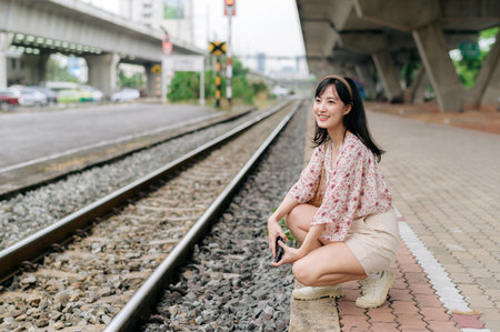 Young Asian woman traveler with weaving basket using a mobile phone beside railway train station in...