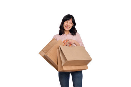 Young happy asian woman with casual shirt and denim jeans holding shopping paper bag on white background.の写真素材