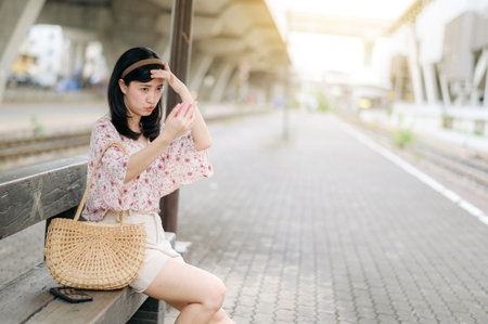 young asian woman traveler checking her face in a mirror and waiting for train in train station. Journey trip lifestyle, world travel explorer or Asia summer tourism concept.の写真素材