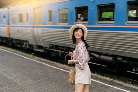 asian young woman traveler with weaving basket looking back happy smiling to a camera beside train coming background. Journey trip lifestyle, world travel explorer or Asia summer tourism concept.の写真素材