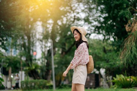 Portrait of young asian woman traveler with weaving hat and basket happy smile on green public park nature background. Journey trip lifestyle, world travel explorer or Asia summer tourism concept.の写真素材