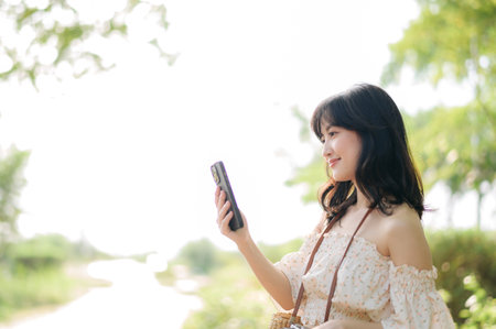 Portrait of young asian woman traveler with weaving hat, basket, mobile phone and camera on green public park background. Journey trip lifestyle, world travel explorer or Asia summer tourism concept.の写真素材