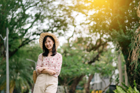Portrait of young asian woman traveler with weaving hat and basket happy smile on green public park...